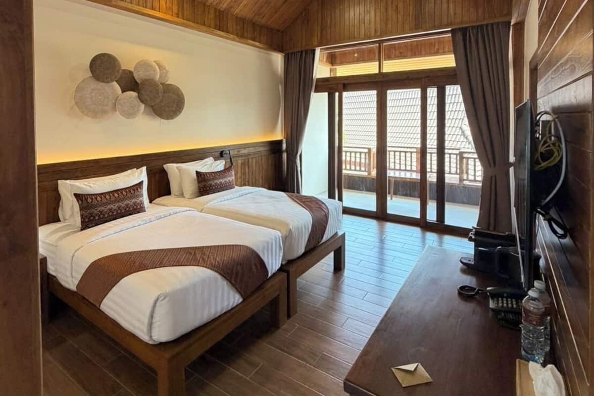 Een slaapkamer met houten lambrisering, twee bedden, een klein bureau en een groot raam.