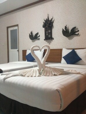 A hotel room with two beds, a wooden headboard, decorative wall art, and a heart-shaped towel arrangement.