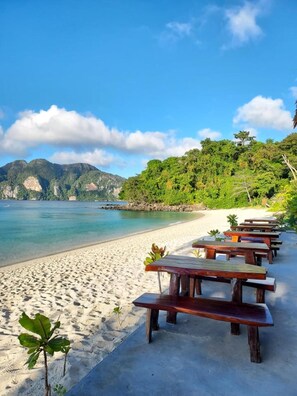 A beach with wooden picnic tables and a clear view of the ocean and mountains. - Paradise Pearl Bungalows (Ko Phi Phi)