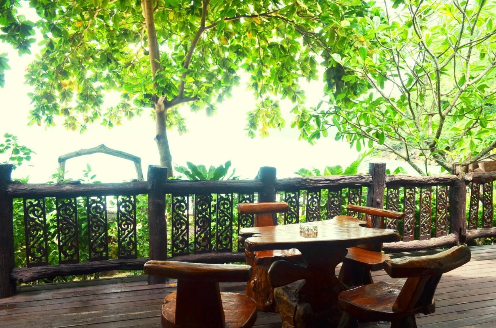 A wooden deck with a table and chairs, surrounded by a decorative fence and lush greenery.