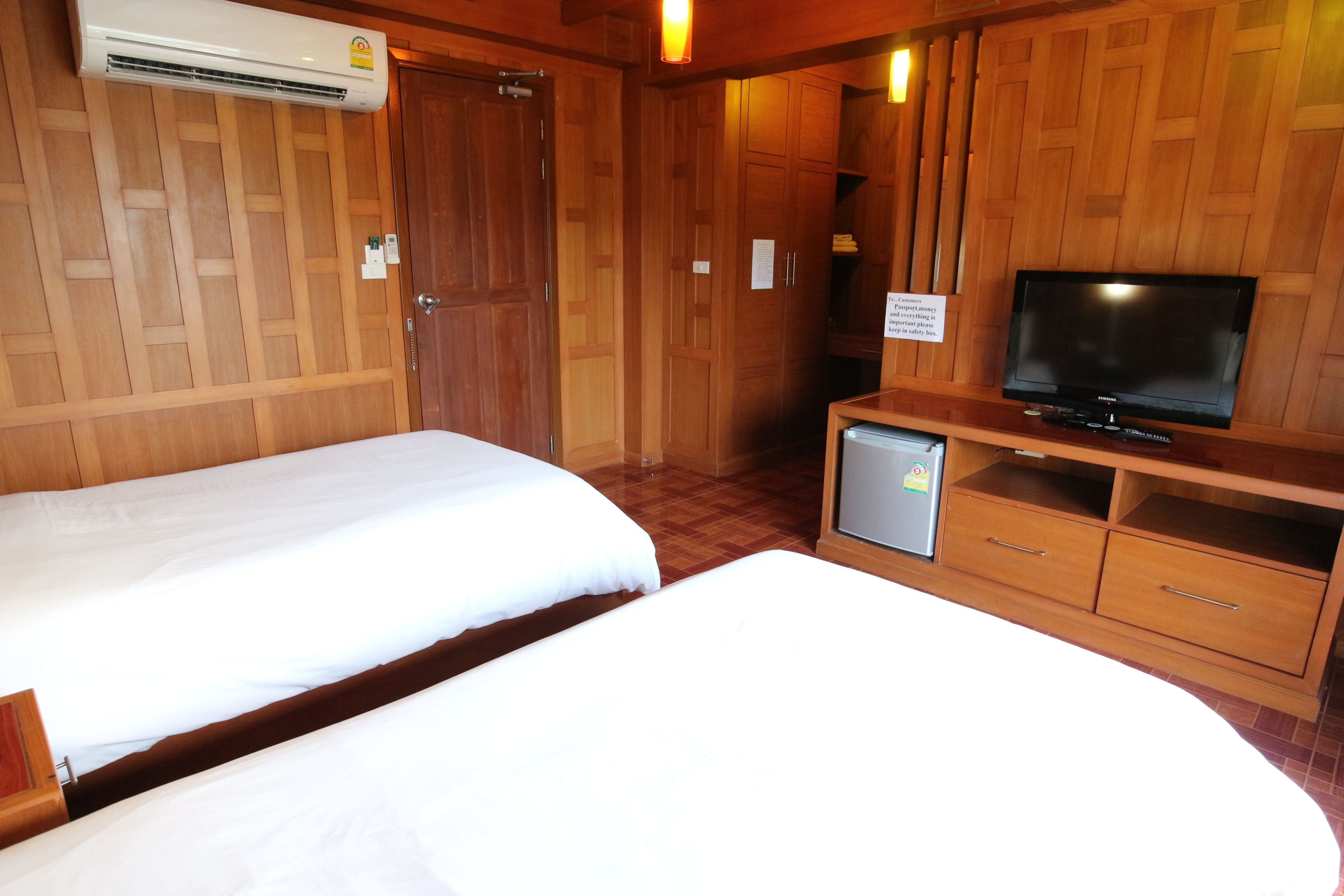 A hotel room with two beds, a TV, a small fridge, wooden paneling, and a sign on the wall.
