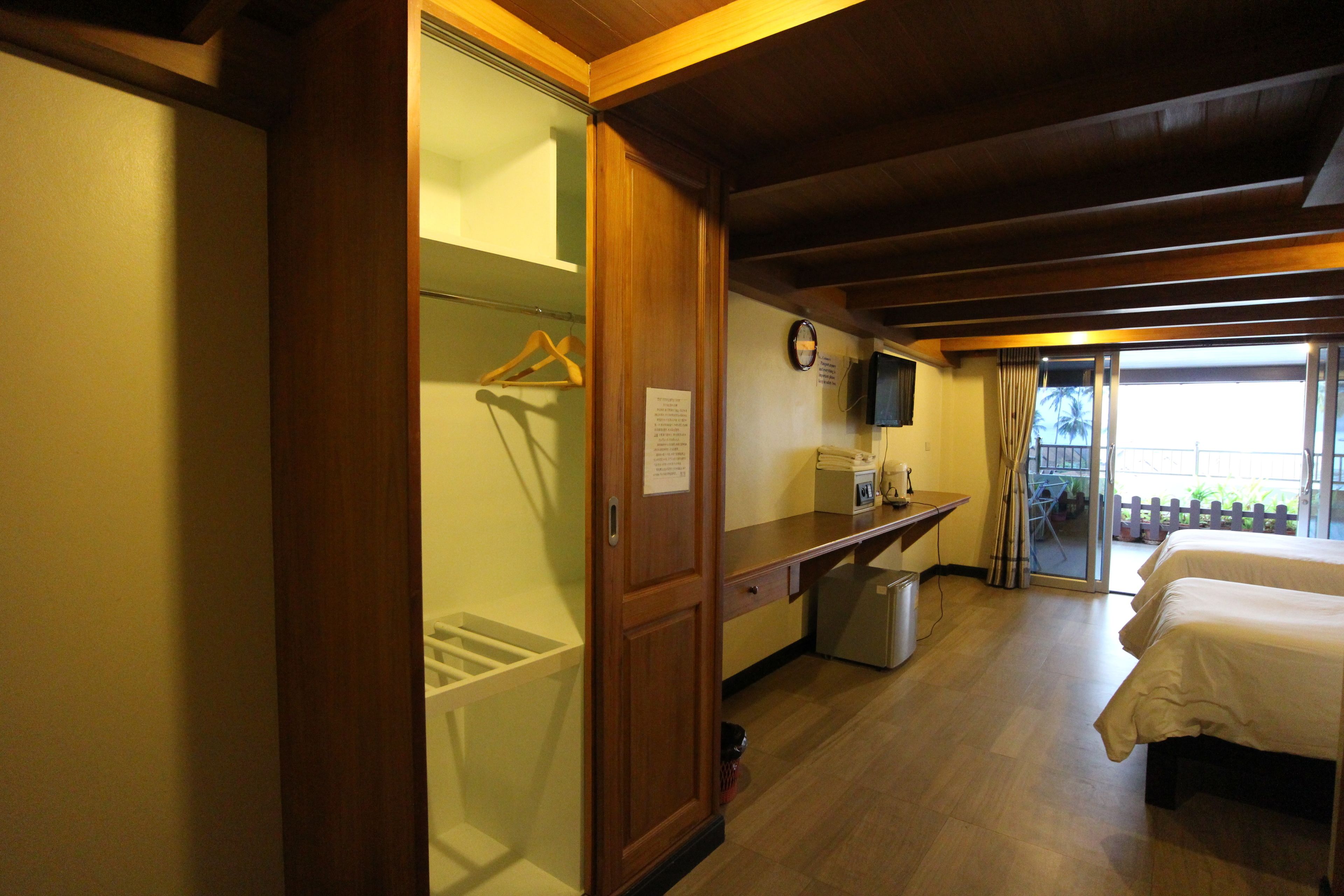 A hotel room with a wooden wardrobe, a desk with a chair, a bed, a television, and a view of the outside.