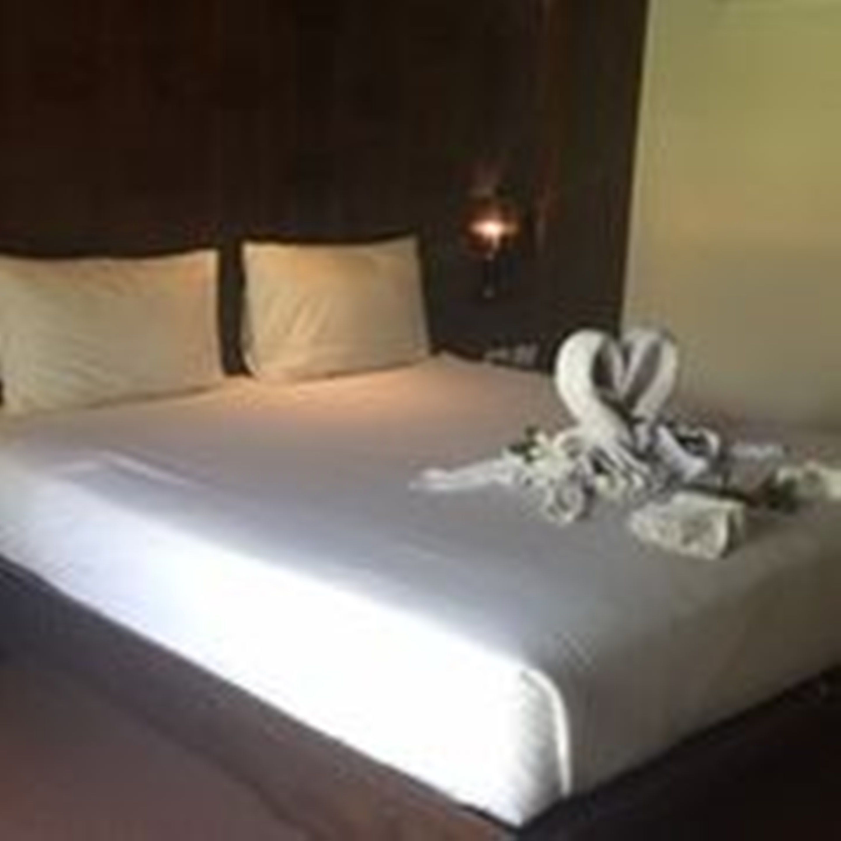 A neatly made bed with pillows and a towel arrangement on the side.