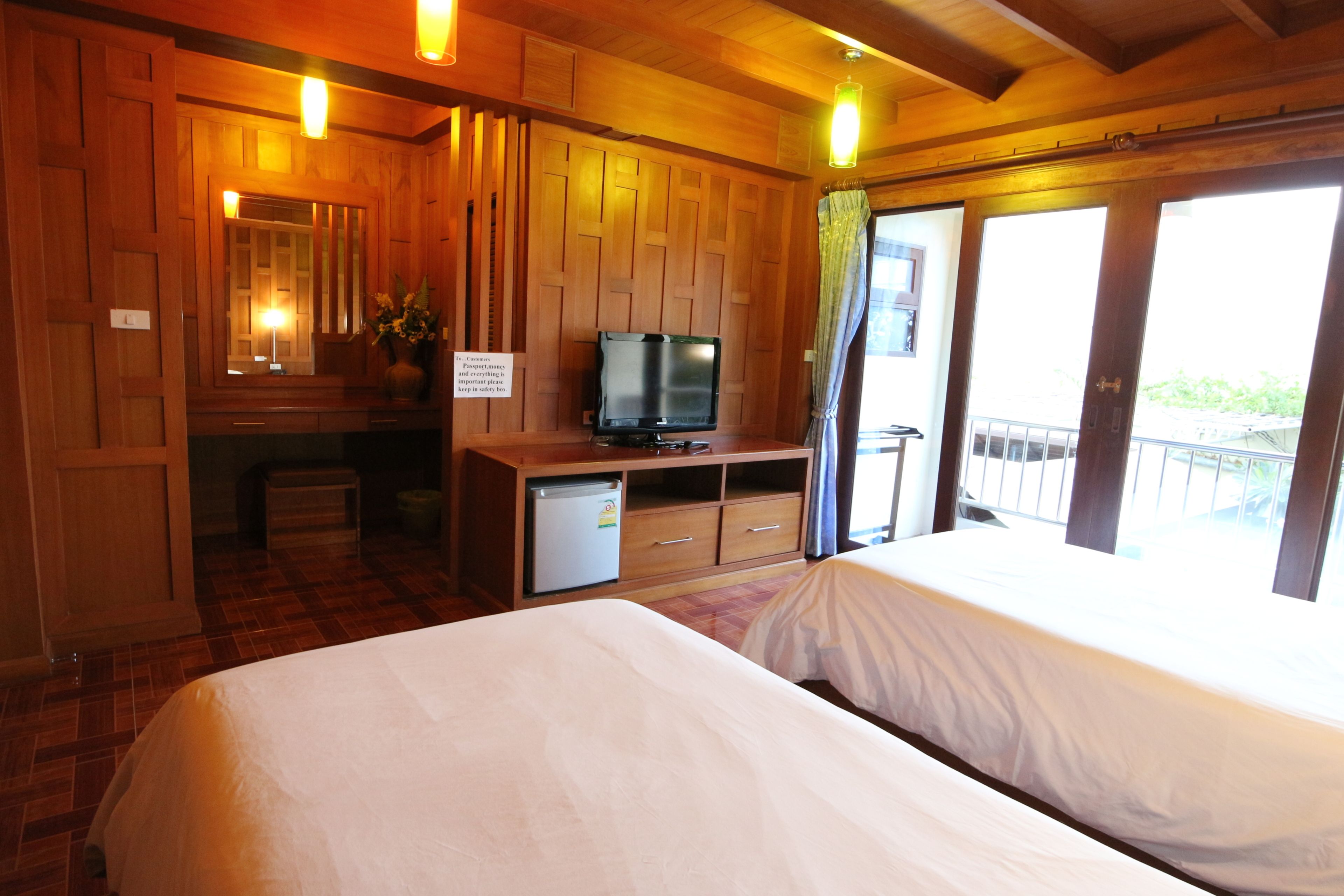A wooden cabin-style room with a bed, a desk with a television, and a balcony with a view.