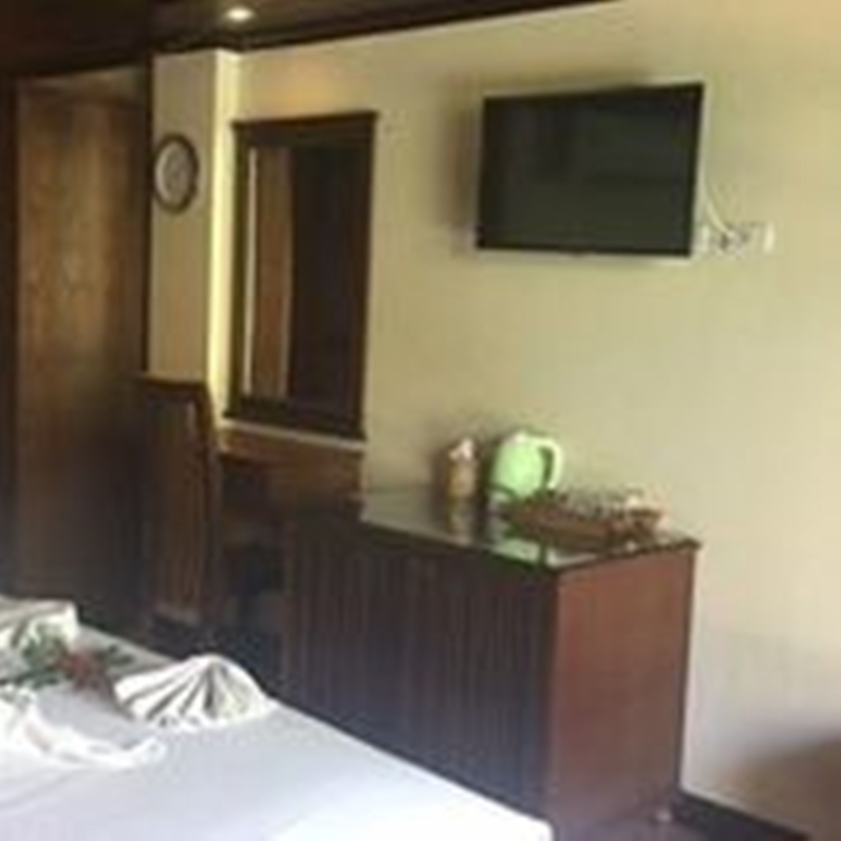 A room with a bed, a wooden desk, a television mounted on the wall, and a clock on the wall.