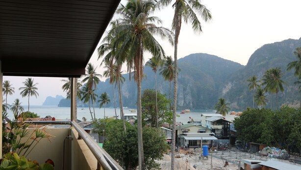 A view from a balcony overlooking a beach with palm trees and a mountainous backdrop. - JJ Residence (Ko Phi Phi)