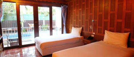 Habitación de hotel con dos camas, paneles de madera en la pared, puerta de cristal corredera hacia un balcón y una pequeña mesa con sillas.