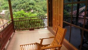 A wooden chair and table on a balcony with a view of greenery.