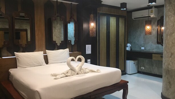 A hotel room with a large bed, a wooden bench, a wall-mounted air conditioner, and a small window.