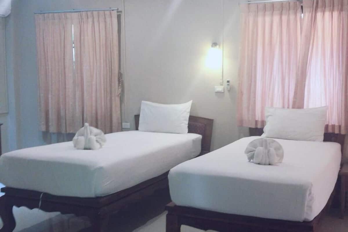 Dos camas individuales con sábanas y almohadas blancas, un cabecero de madera, una lámpara de pared y una ventana con cortinas.