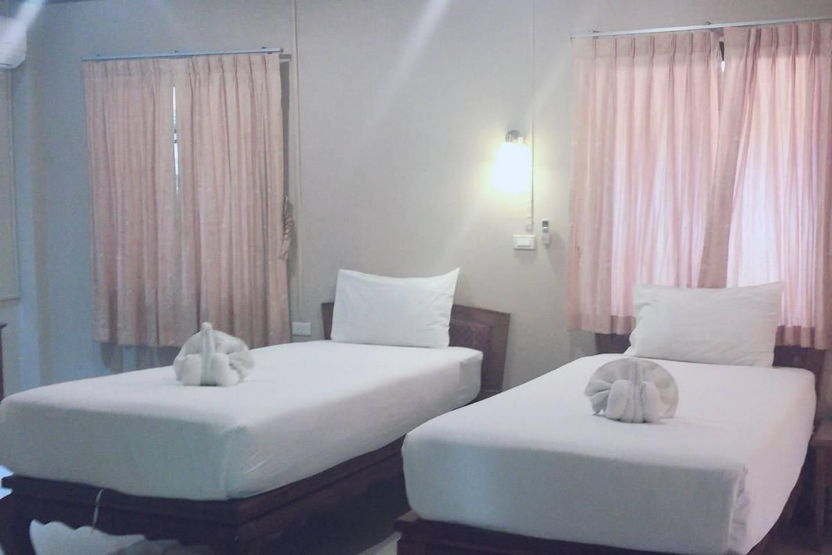 Dos camas individuales con ropa blanca, cabeceros de madera y una lámpara de pared.