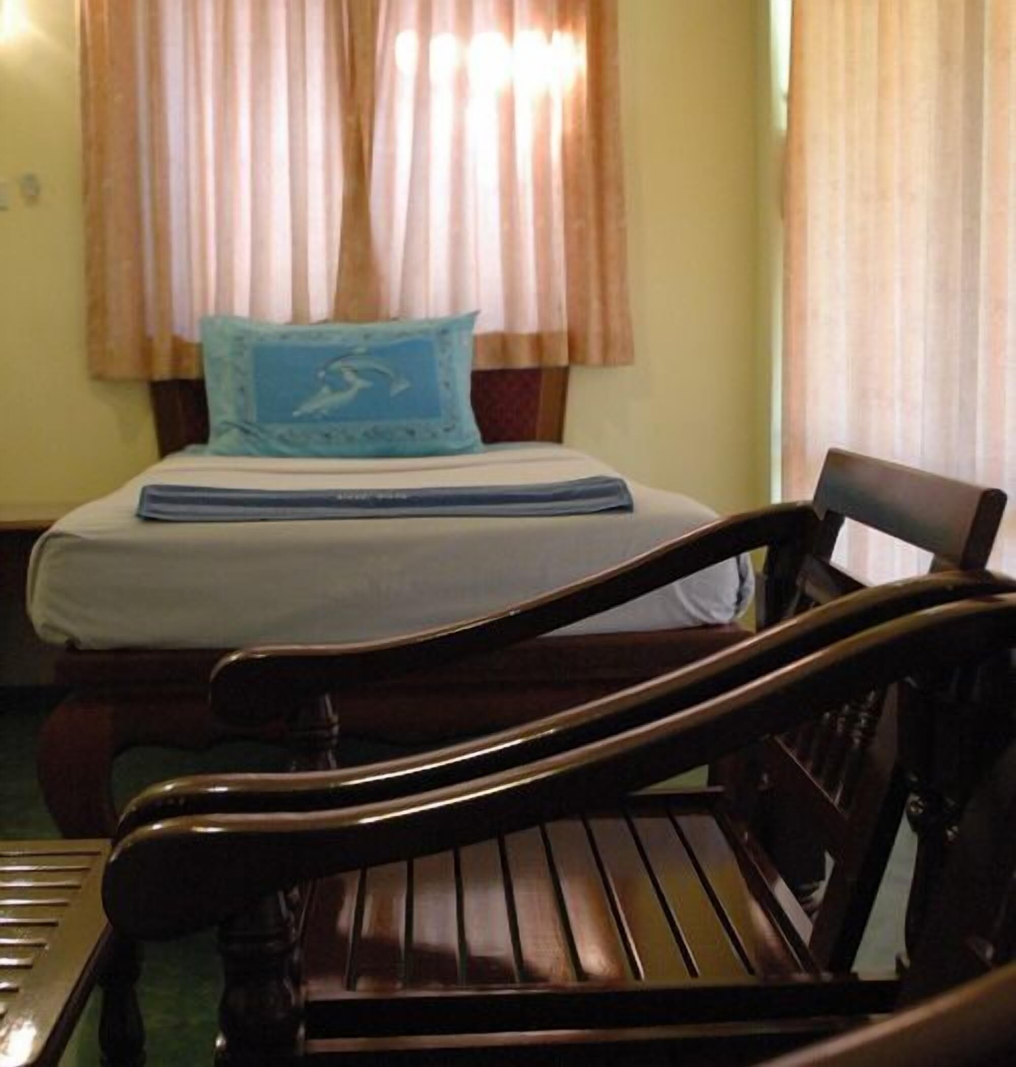 A room with a bed, a wooden chair, and a window with curtains.