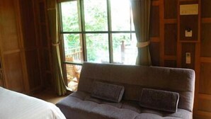 A room with a large window, wooden walls, and a grey sofa with cushions.