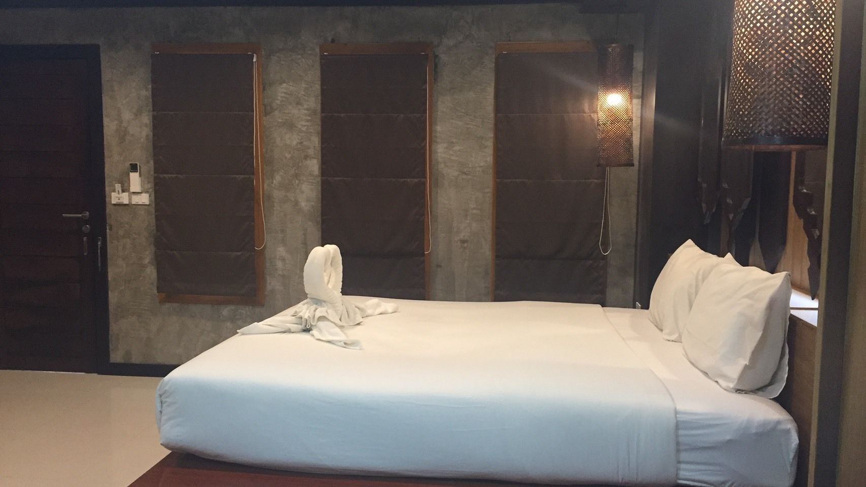 A hotel room with a large bed, two windows, a wall-mounted lamp, and a door.