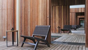 Een houten terras met een rij zwarte ligstoelen en een klein tafeltje.