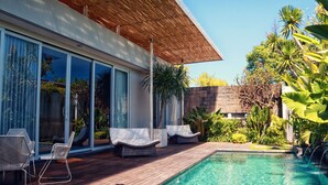 Een modern buitenzwembad met ligbedden, een houten terras en een patio met glazen wanden.