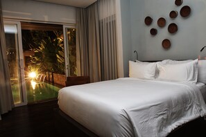 A bedroom with a large bed, a sliding glass door leading to a pool, and a wall with circular decorations. - Hu'u Villas (Seminyak)