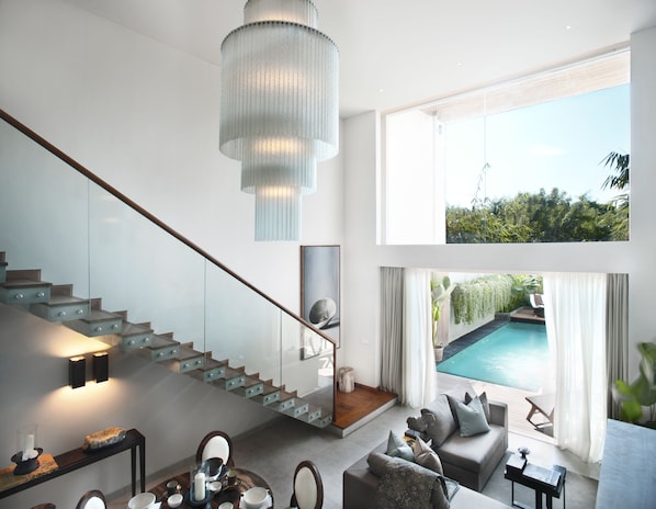 A modern interior with a staircase, a pool, and a large window offering a view of greenery. - Hu'u Villas (Seminyak)