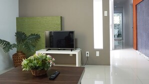A modern living room with a flat-screen TV on a white stand, a wooden coffee table with a plant and remote, and a large window. - Forest View Leisure Residences (Morong)