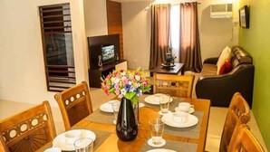 A dining area with a table set for four, a vase of flowers, and a television in the background. - Forest View Leisure Residences (Morong)