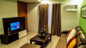 A living room with a flat-screen TV, a sofa, a coffee table, and a decorative vase. - Forest View Leisure Residences (Morong)