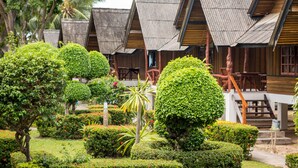 A row of traditional wooden huts with thatched roofs, surrounded by well-maintained gardens and palm trees. - Shangrilah Bungalow (Koh Samui)