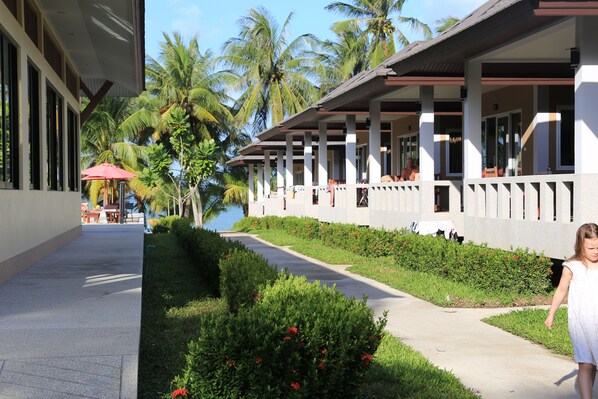A hotel corridor with a pathway, palm trees, and a view of the sea.