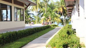 A pathway lined with greenery and palm trees, leading to a building with large windows and a covered area. - Shangrilah Bungalow (Koh Samui)