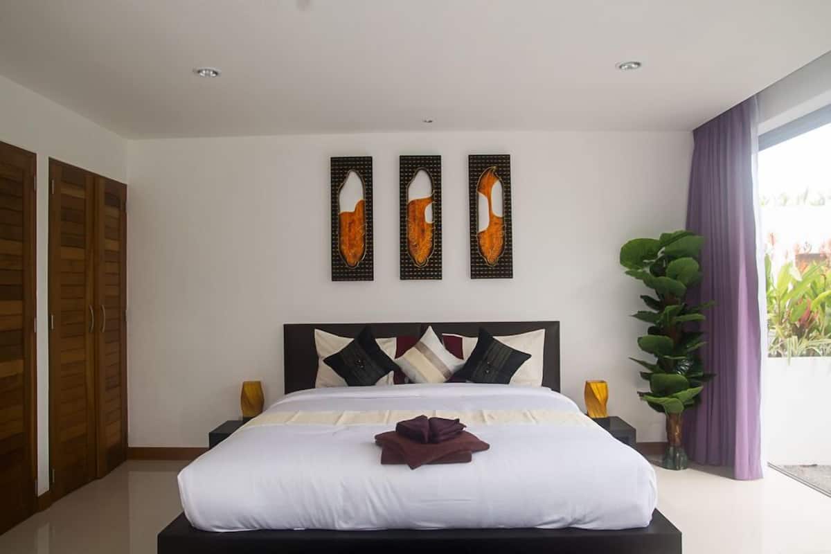 Habitación de hotel con una cama grande, un armario de madera y vistas a zonas verdes por la ventana.
