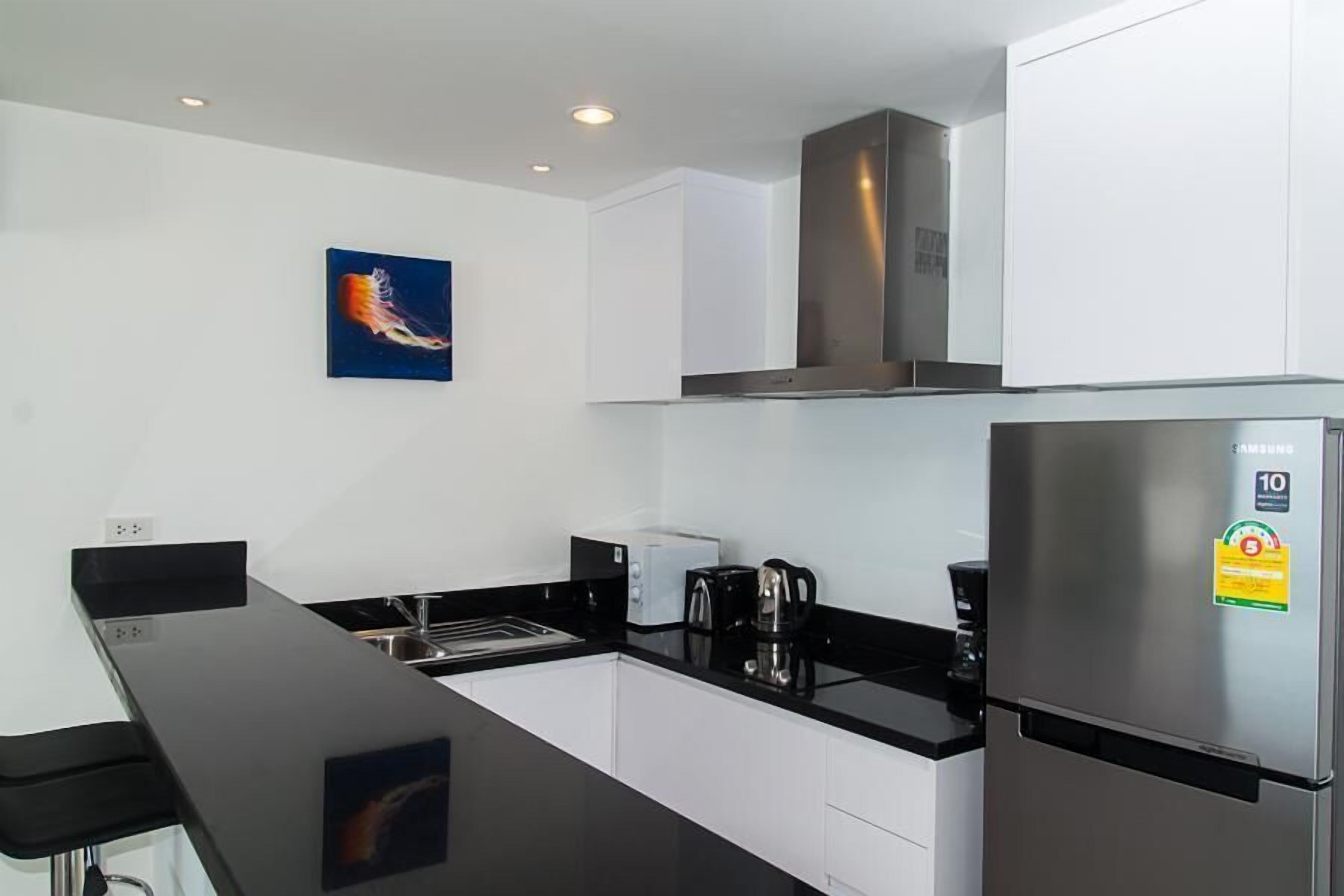 A modern kitchen with white cabinets, a black countertop, a stainless steel refrigerator, and a coffee maker.