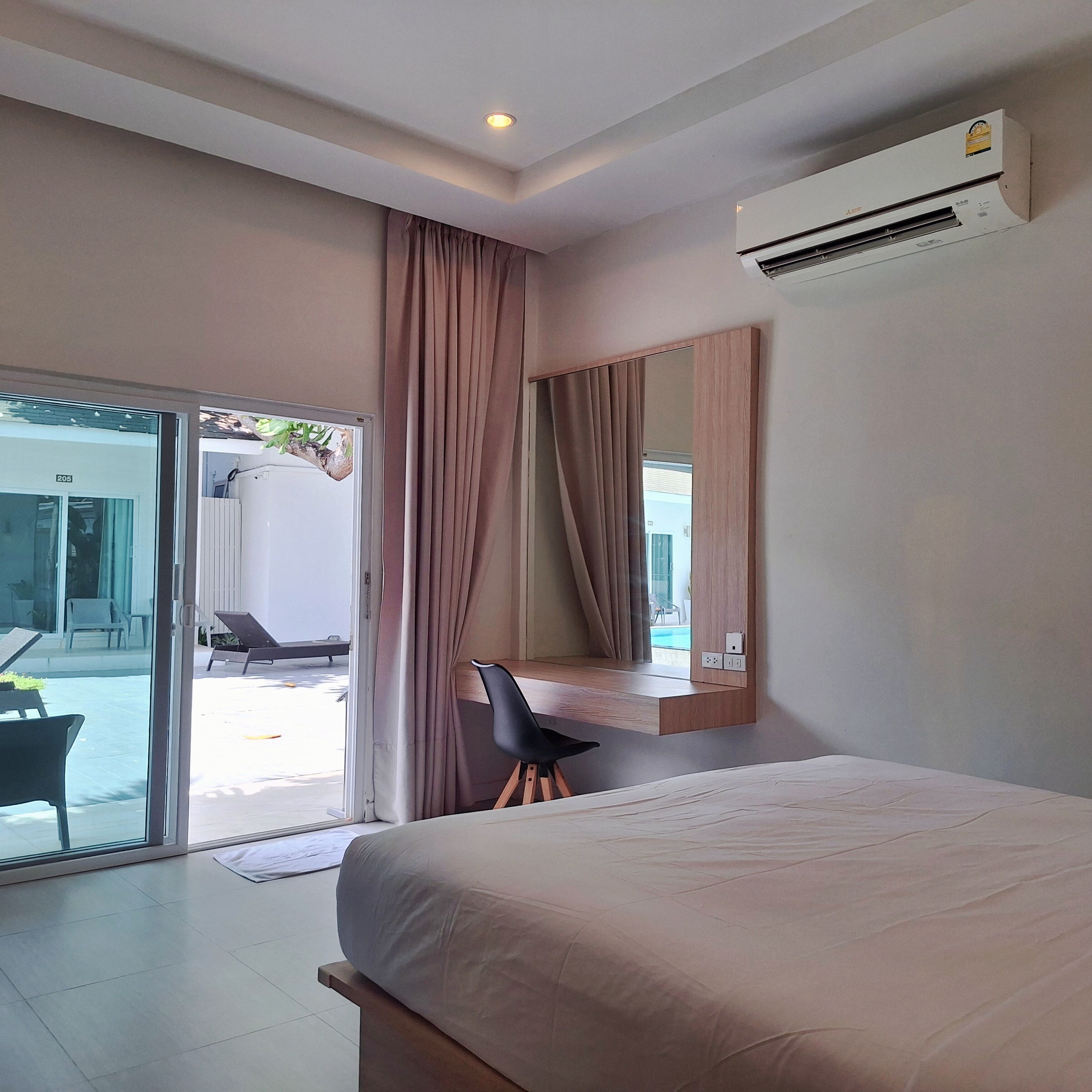 Una habitación de hotel moderna con una cama grande, un escritorio, una silla y un ventanal corredero que da a un espacio exterior.