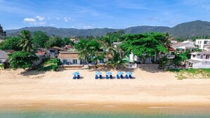 A beachside property with a row of blue umbrellas, a sandy beach, and a backdrop of mountains and trees. - Baan Fah Resort (Koh Samui)