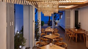 A modern restaurant interior with wooden tables and chairs, a woven ceiling light fixture, and a view of the outdoors. - Baan Fah Resort (Koh Samui)