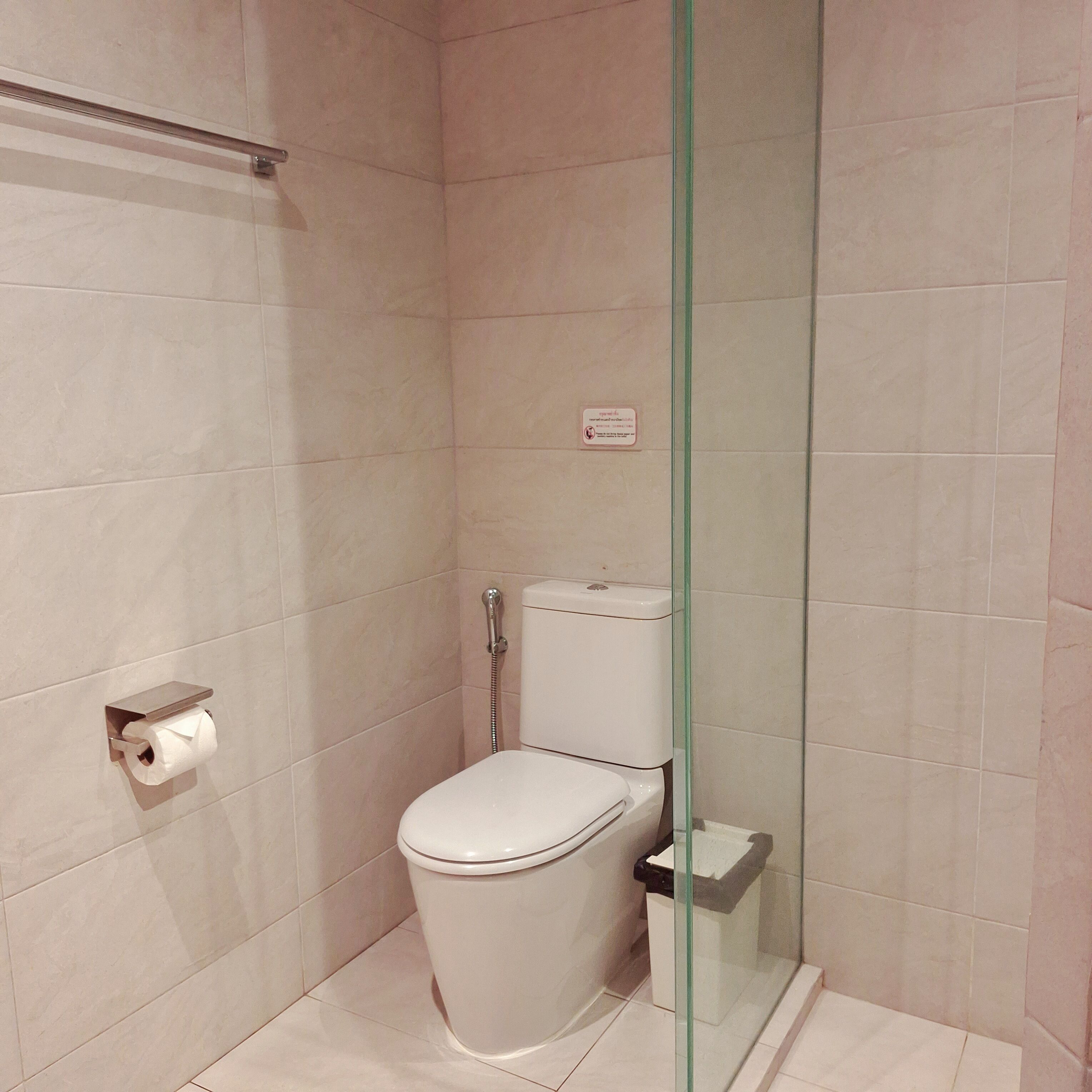 A modern bathroom with a glass shower enclosure, a toilet, and a paper towel dispenser.