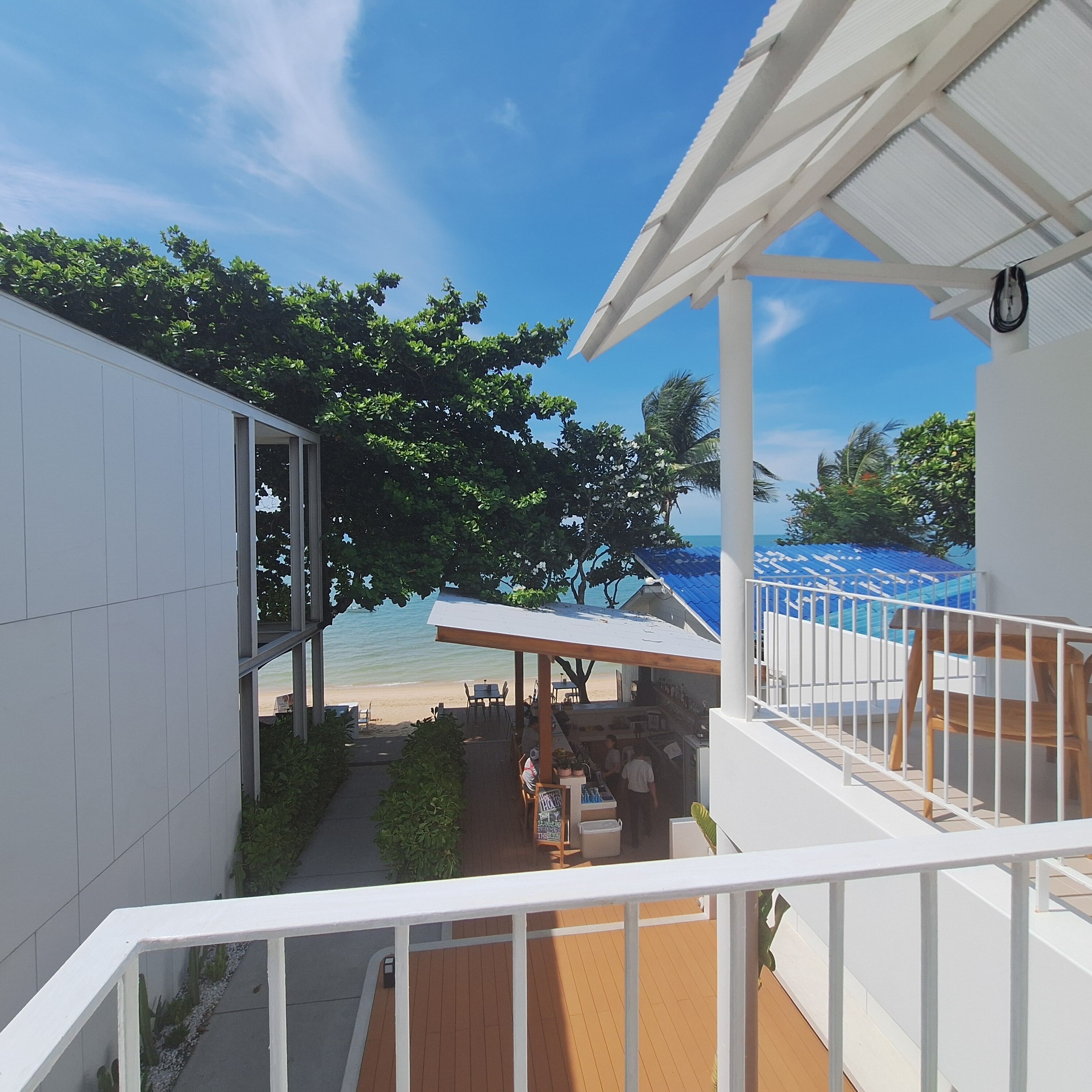 Un balcone con vista sulla spiaggia, una zona salotto all'aperto coperta e un edificio bianco.
