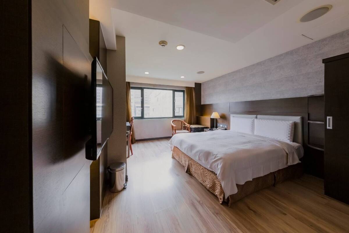A modern hotel room with a large bed, a TV, a desk, and a chair.