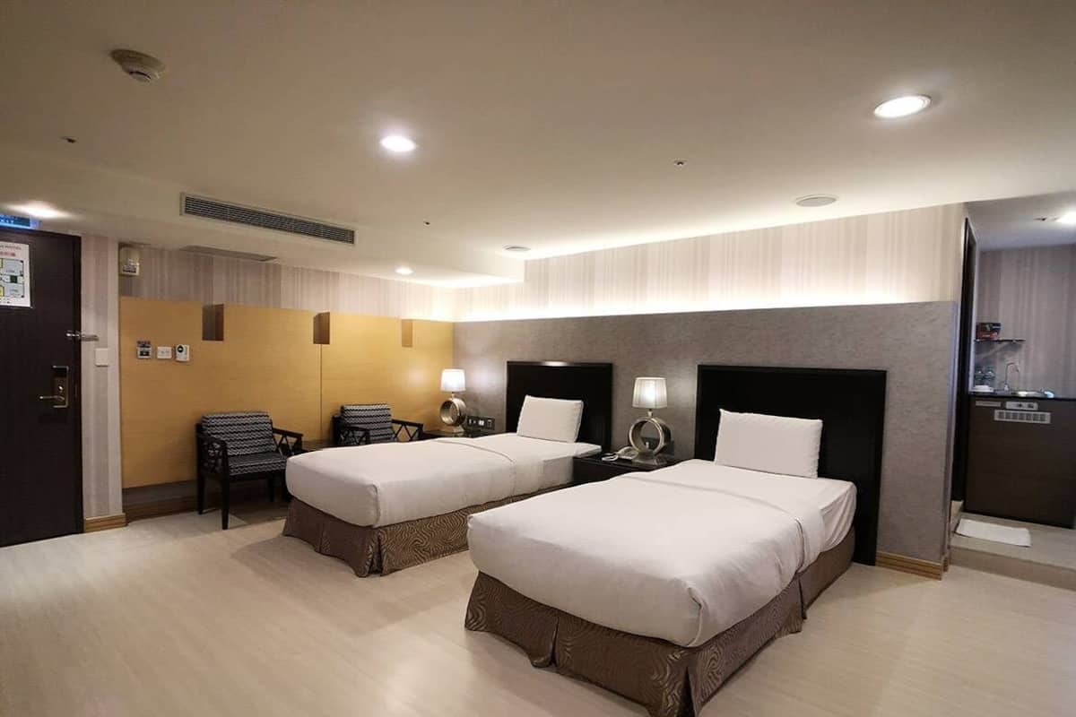 A hotel room with two beds, a desk, a chair, a TV, and a minibar.