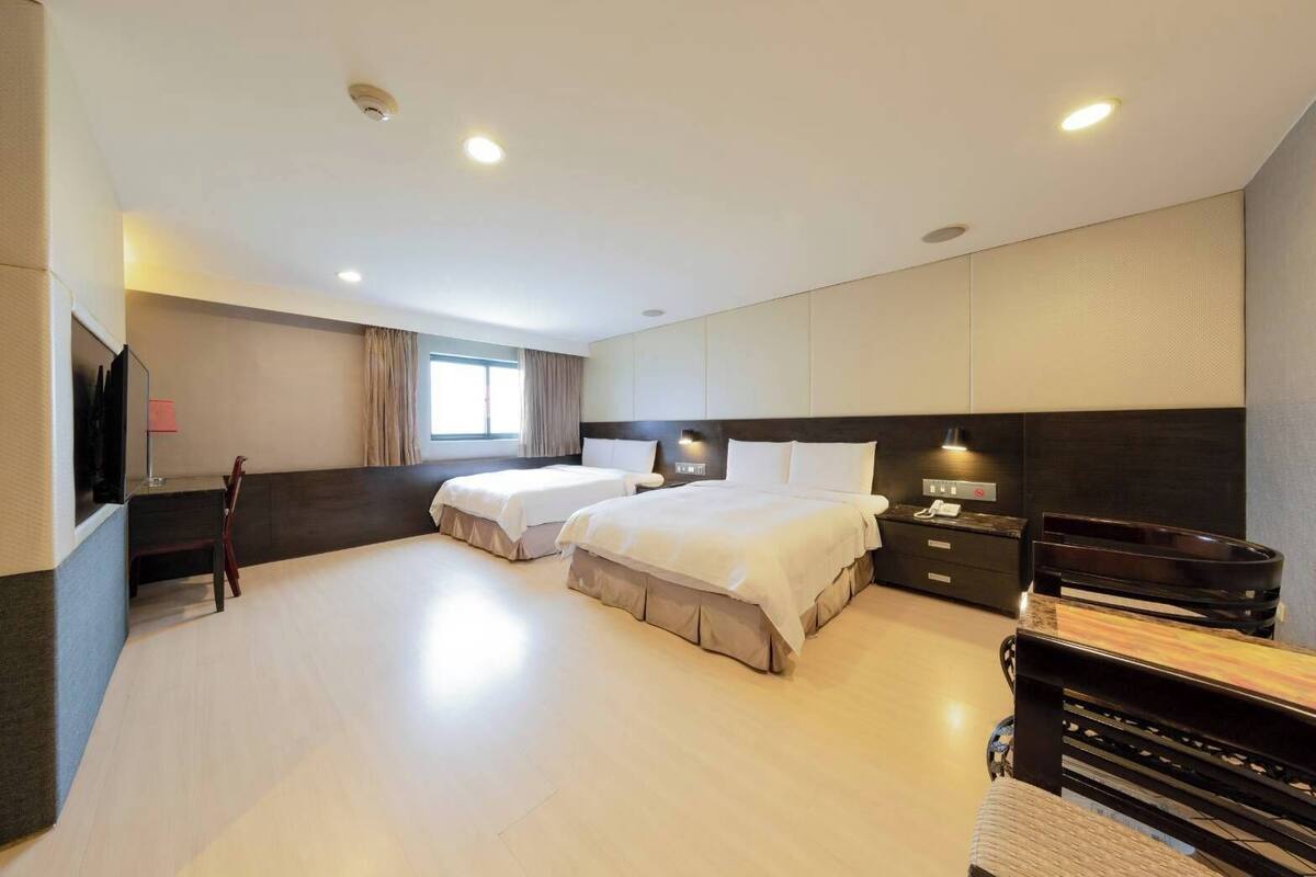A hotel room with two beds, a desk, a TV, and a minibar.