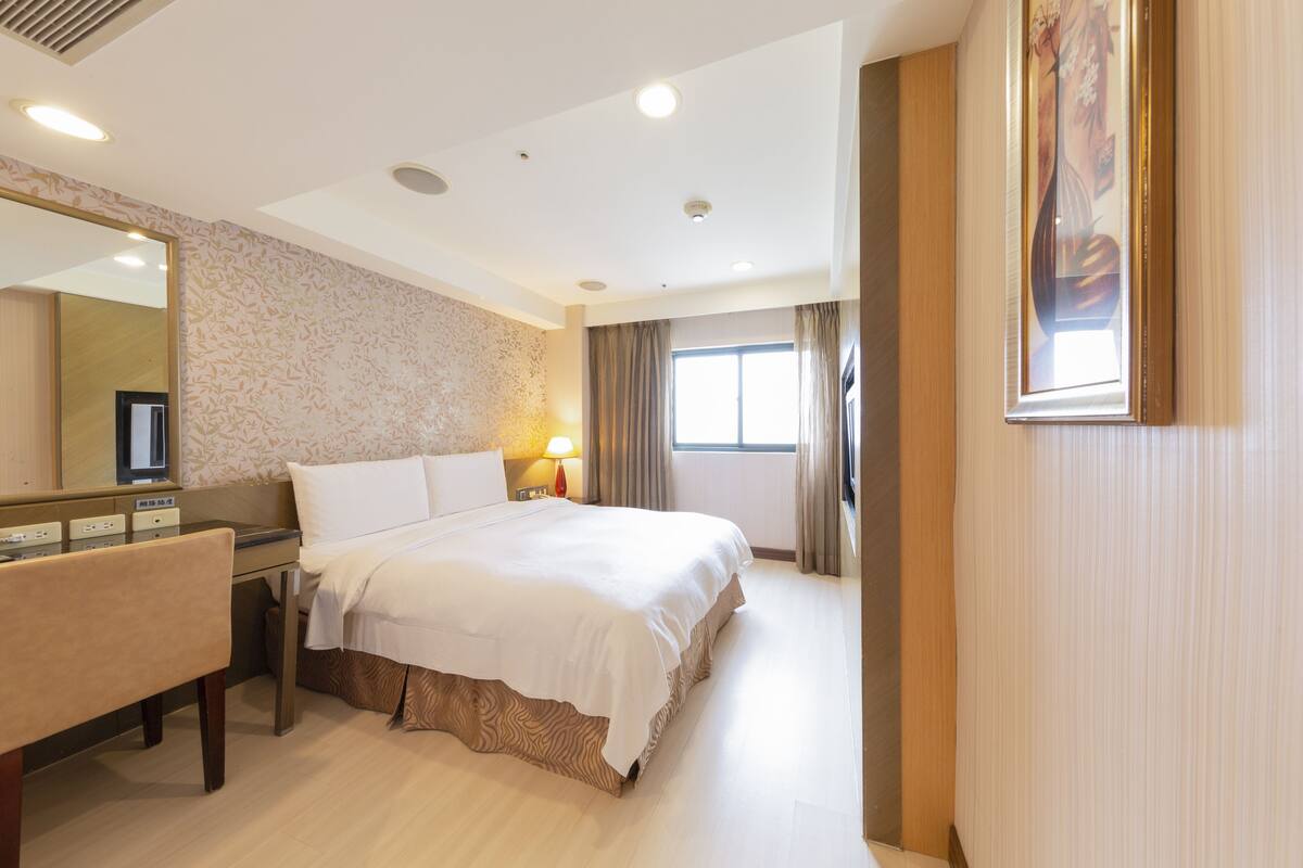 A hotel room with a bed, bedside table, lamp, and a large mirror.
