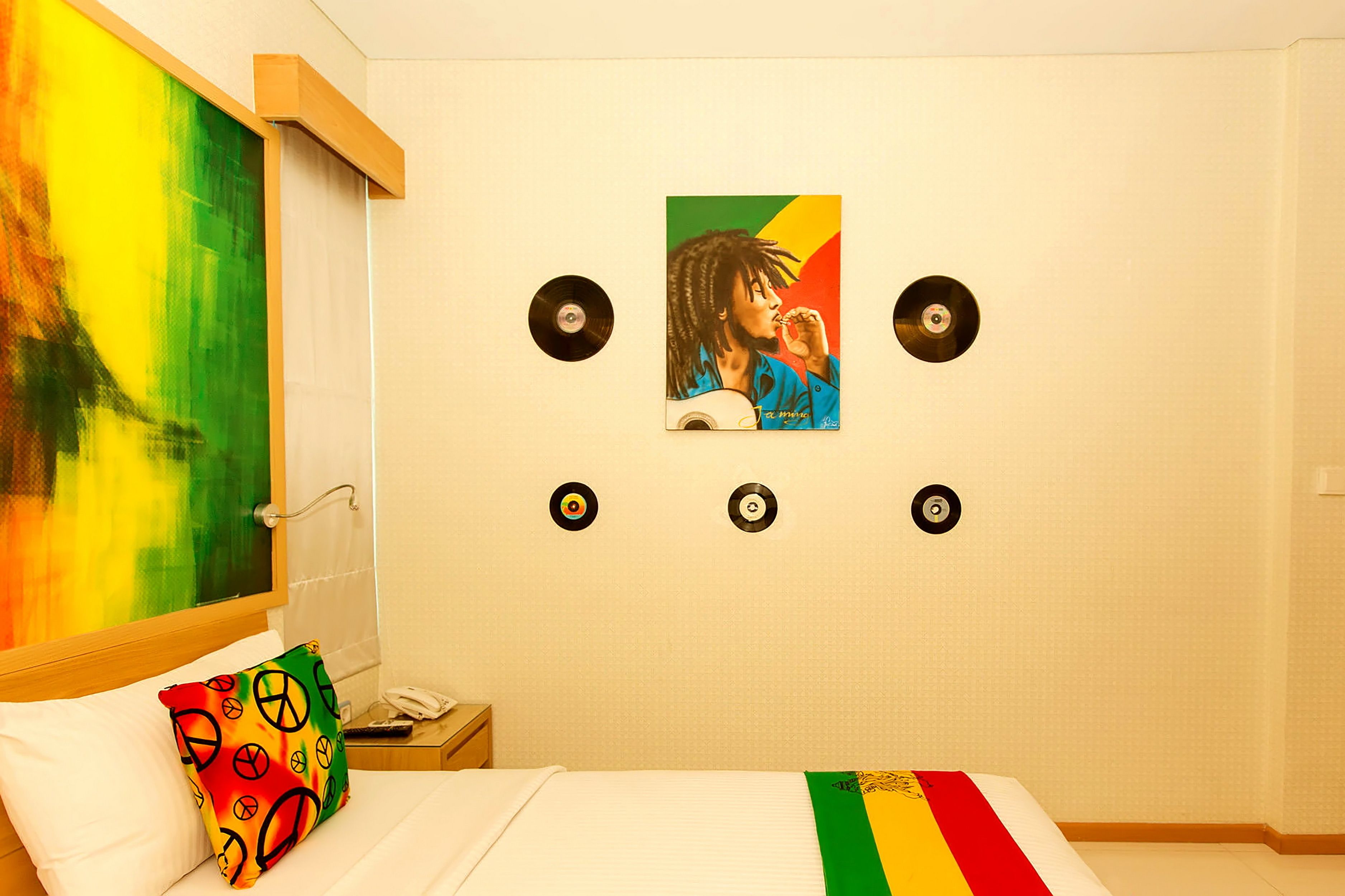 A hotel room with a bed, a colorful pillow, a painting on the wall, and three vinyl records.