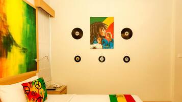 A hotel room with a bed, a colorful pillow, a painting on the wall, and three vinyl records.
