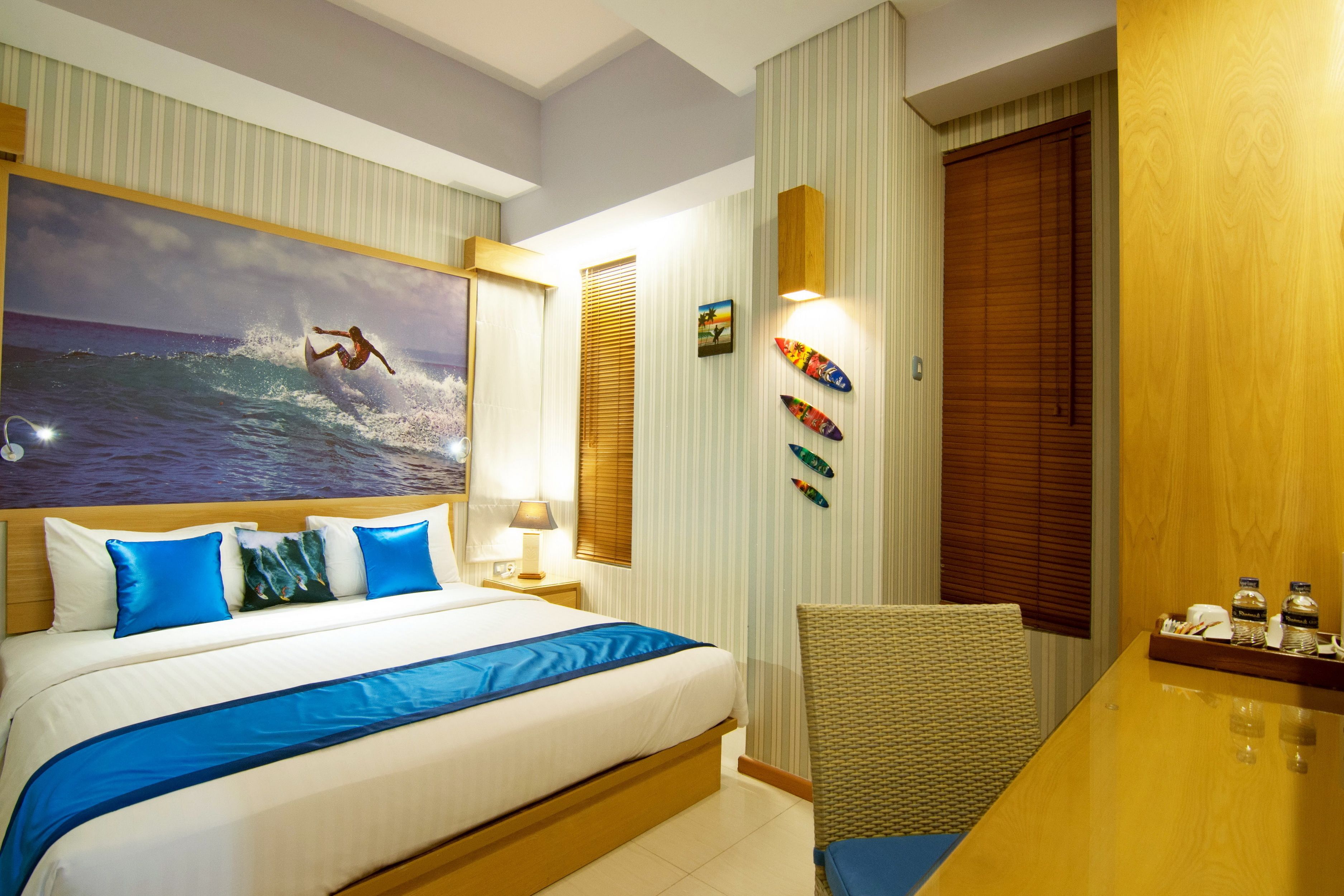 A hotel room with a bed, a desk, and a wall with surfboards.