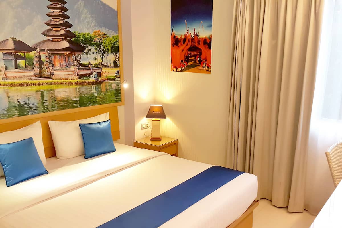 A hotel room with a bed, a nightstand, a lamp, and two paintings on the wall.