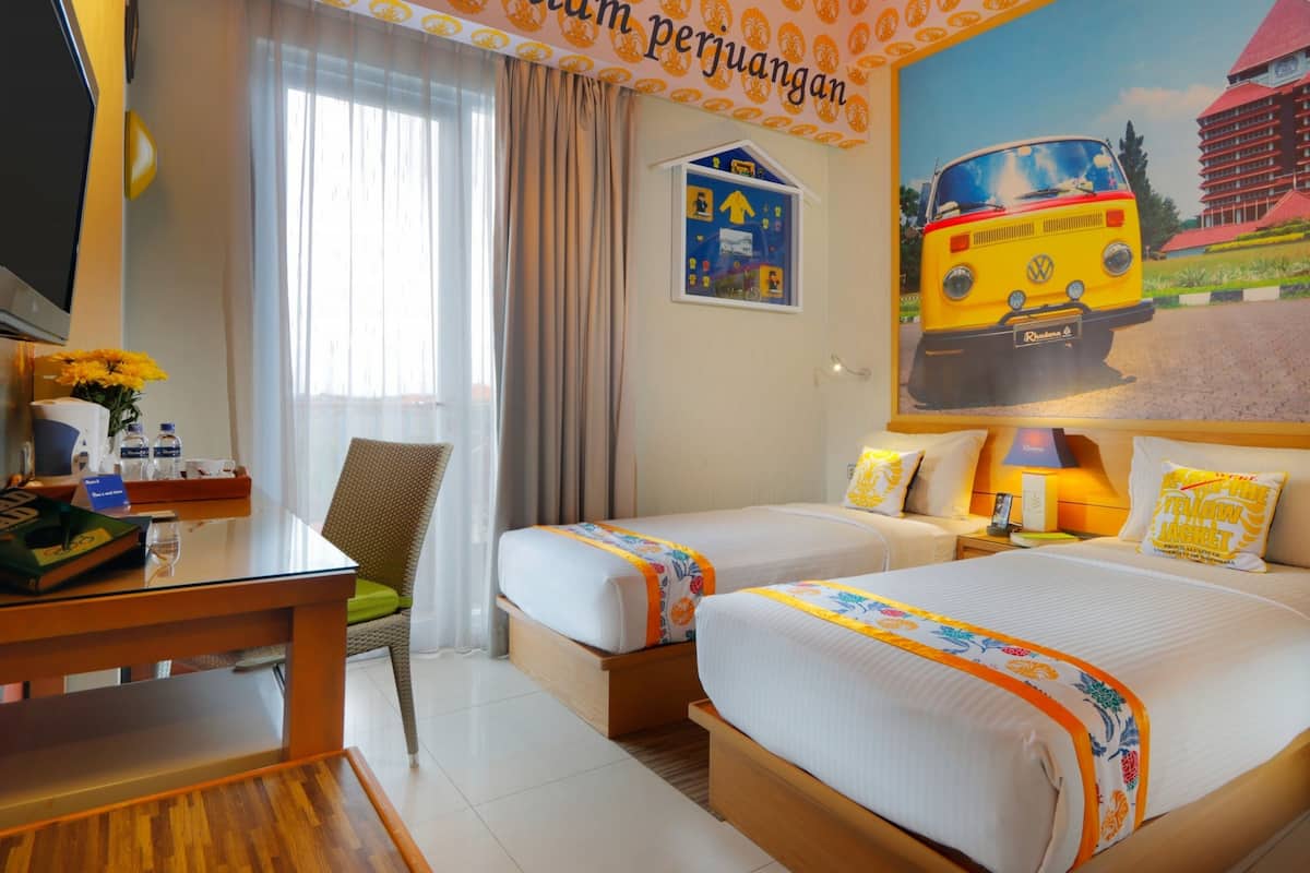 A hotel room with two beds, a desk, a chair, a TV, and a large window with curtains.