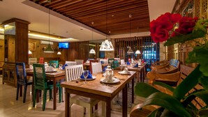 Zona pranzo con tavoli e sedie di legno, televisore e illuminazione decorativa.
