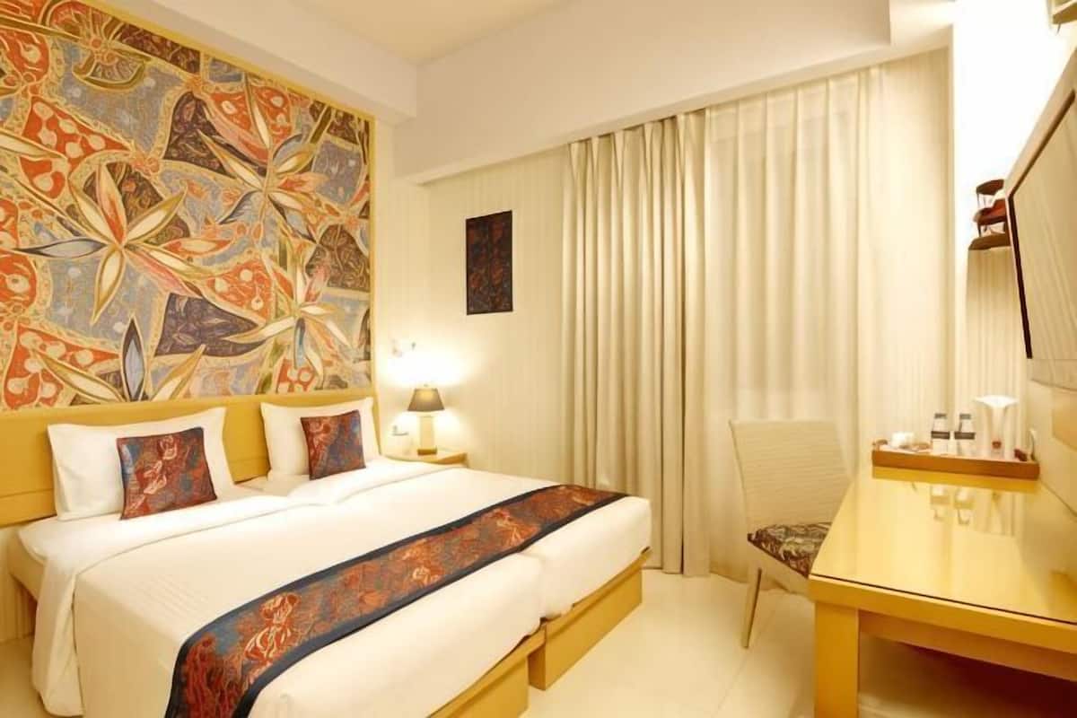 A hotel room with a large bed, a bedside table, a chair, a desk, and a large mirror.