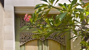 A traditional wooden door with intricate carvings, flanked by two statues, and a garland of marigolds at the base. - Elok Villas (Seminyak)