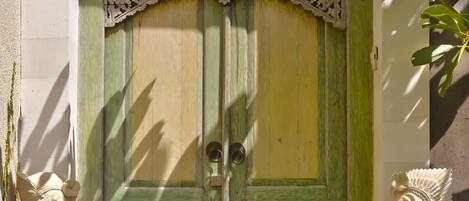 A traditional wooden door with intricate carvings, flanked by two statues, and a garland of marigolds at the base.