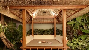 A wooden bed with a thatched roof, surrounded by lush greenery. - Elok Villas (Seminyak)