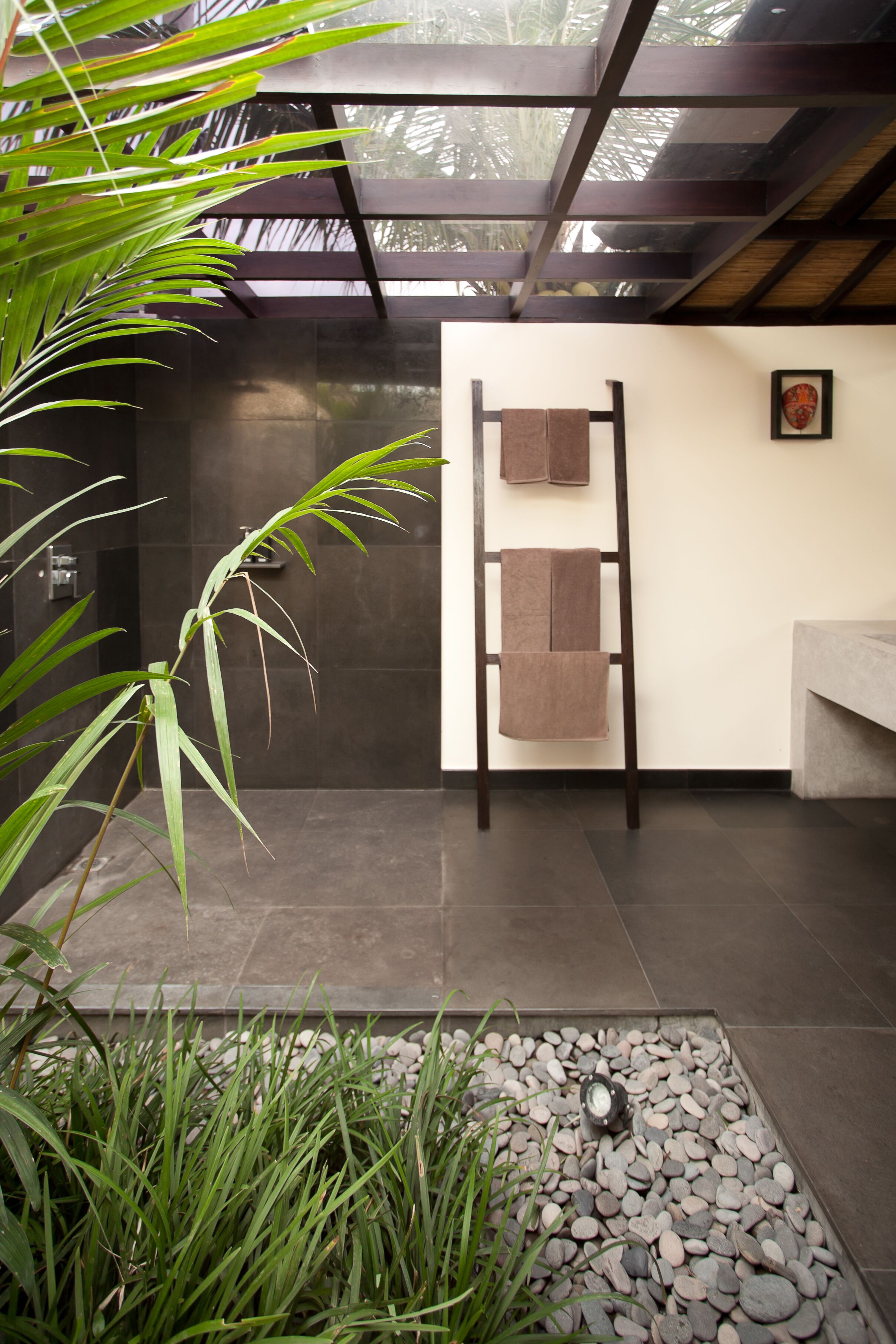 A modern bathroom with a wooden ladder, towels, and a stone floor.